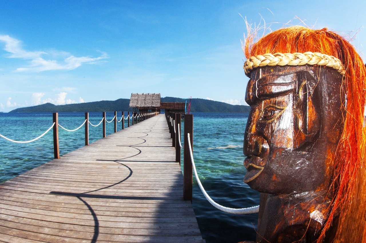 face of a wooden papuan statue with Papua Explorers main jetty in the backgound