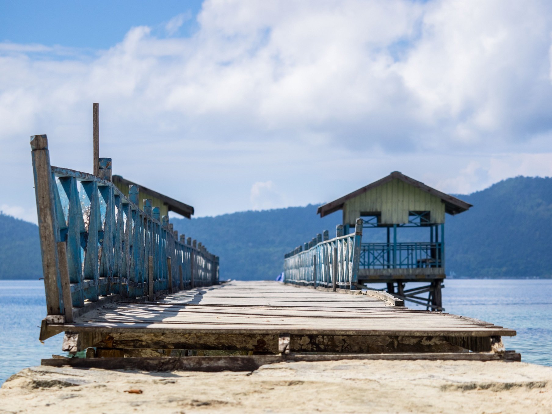 (English) blue painted wooden jetty with two huts on the sides close to Papua Explorers Dive Resort