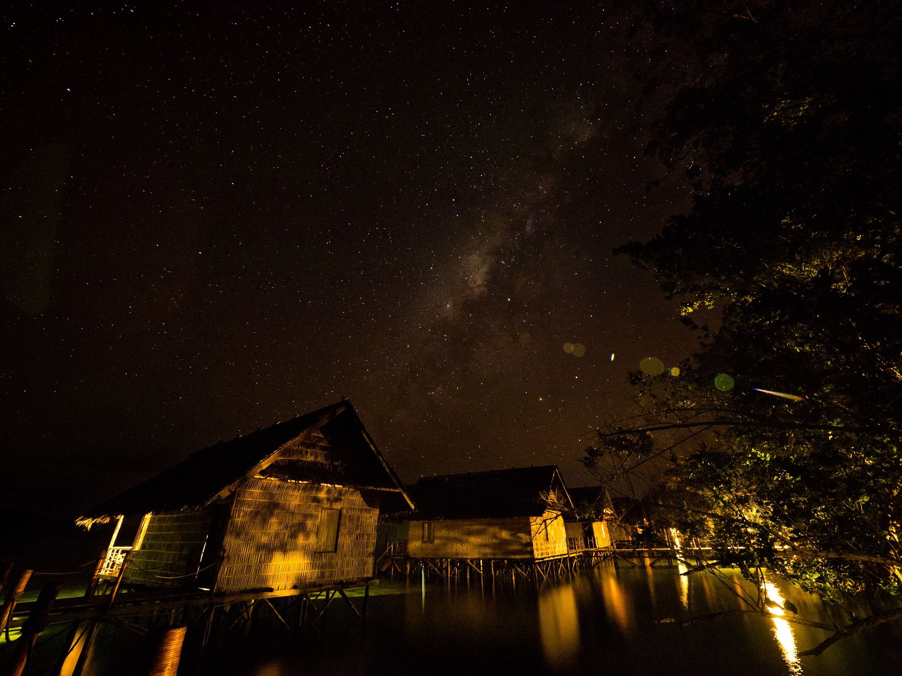 star-filled firmament above the well lit over water cottages of our Raja Ampat dive resort