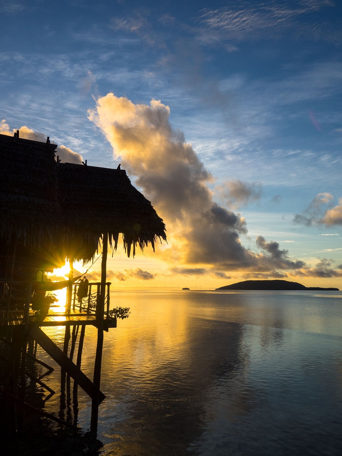 (English) view of kri island and the sun rising above the sea shining through the veranda of one of our water cottages at our dive resort in Raja Ampat
