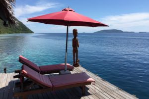 sunloungers and red umbrella and a wooden papuan statuse at our dive centre facing the ocean