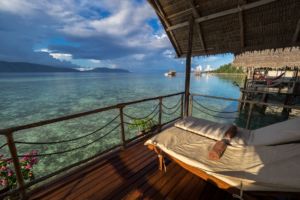 view from the balcony of our water bungalows in Raja Ampat with sun loungers in the front and our dive centre and islands of the Dampier Straight in the back