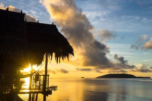 view of kri island and the sun rising above the sea shining through the veranda of one of our water cottages at our dive resort in Raja Ampat