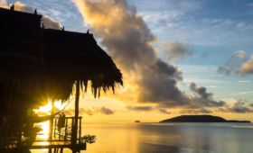 (English) view of kri island and the sun rising above the sea shining through the veranda of one of our water cottages at our dive resort in Raja Ampat