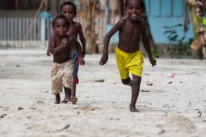 three happy Papuan kids running with village houses in the background