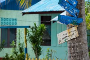 blue painted houses in Arborek with a colorful fence and a tree with signs reminding to treat the reefs with care observed on a break in between dives with Papua Explorers Dive Resort