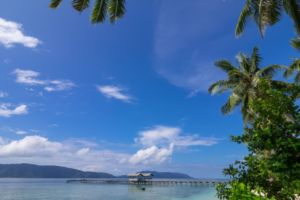 the jetty leading to a village close to Papua Explorers Dive Resort with local boats and beach in the front and island silouettes in the back